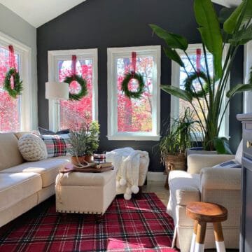 small sunroom decorated for Christmas with a red plaid rug and window wreaths