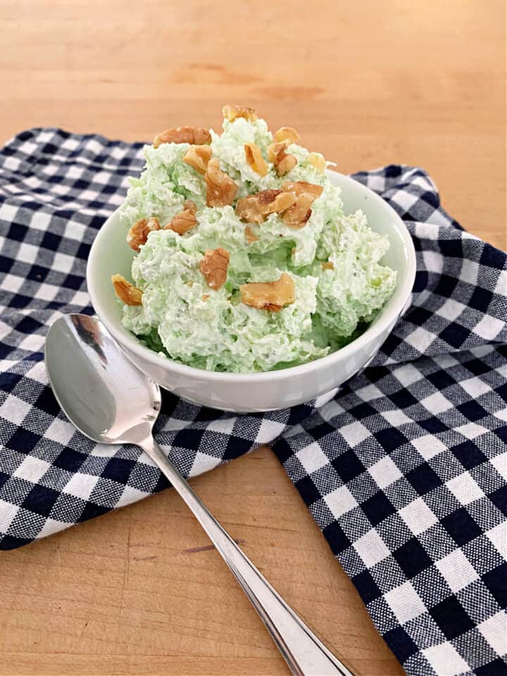 green stuff with walnuts on top in a small white bowl