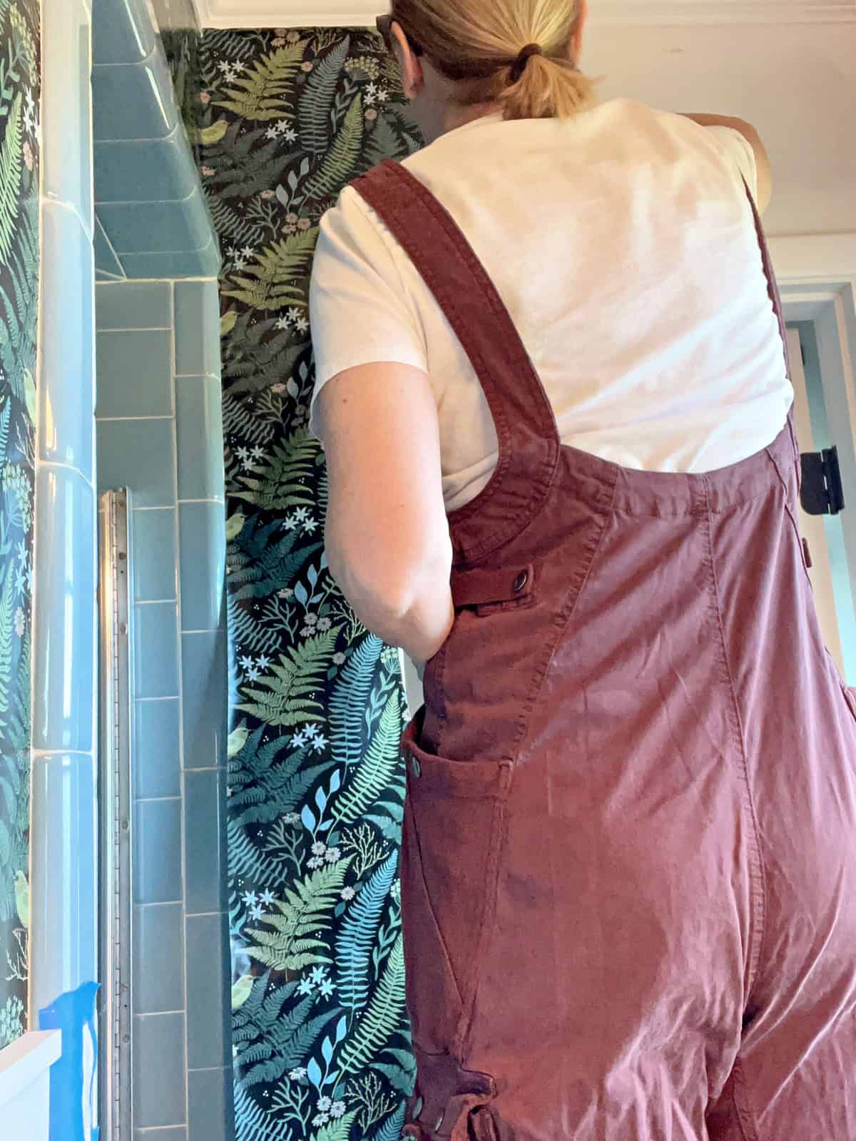 woman in overalls hanging wallpaper in master batroom